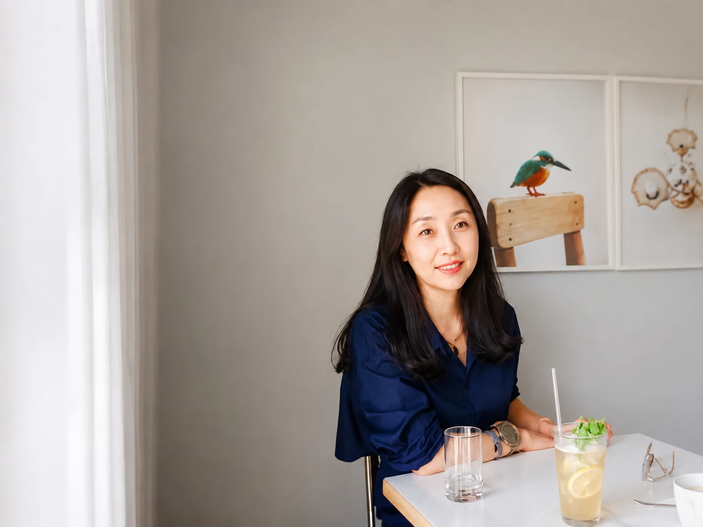 Esther Cho in a navy blouse seated beneath two framed artworks